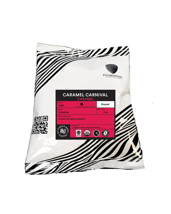 A white bag of Caramel Carnival by Fogbuster® Coffee Works features black zebra stripes and a bright pink label highlighting its caramel flavor, Honduras origin, light roast, ground texture, weight, tasting notes, QR code, and certifications.