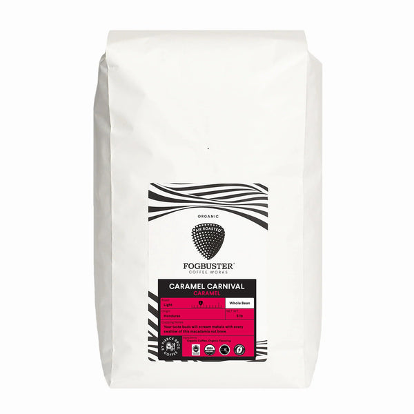 A white bag of Fogbuster® Coffee Works Caramel Carnival whole bean coffee, with black and white stripes and a pink label highlighting its light roast and caramel flavor, made from organic Honduran beans.