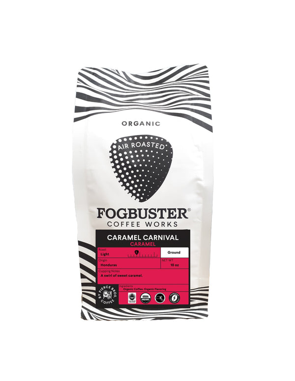 A white bag of Fogbuster® Coffee Works Caramel Carnival features black zebra stripes, a large coffee bean graphic, and a pink label highlighting this light roast caramel-flavored organic ground coffee from Honduras.