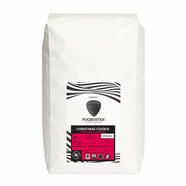 A white bag of Fogbuster® Coffee Works Christmas Cookie organic light roast coffee features a black-and-white striped design and a pink section with tasting notes and roast level details.