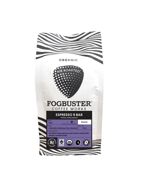 A white bag of Fogbuster® Coffee Works Espresso 9 Bar displays a black and white zebra-stripe design, organic and air roasted labels, and describes its Italian-style espresso with caramel notes from Colombia, Honduras, and Peru.