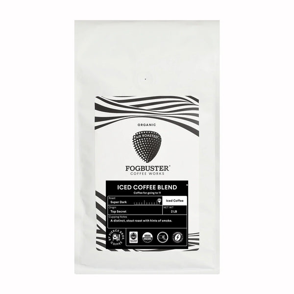A white bag of Fogbuster® Coffee Works Iced Coffee Blend features a black and white label with a strawberry logo, stout roast details, and product information.