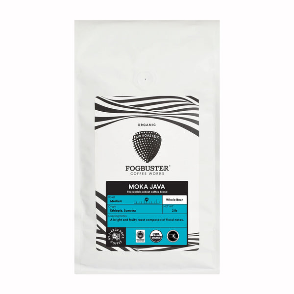 A white bag of Fogbuster® Coffee Works Moka Java whole bean coffee features a black-striped design and certification logos. The label notes it’s organic, medium roast Ethiopian coffee with fruity notes from Ethiopia and Sumatra.