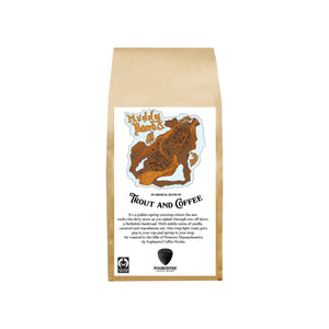 A brown paper bag of Muddy Boots by Trout & Coffee features a fish illustration. This fresh light roast coffee offers caramel and nut flavors, with certifications and roasting info listed on the label.