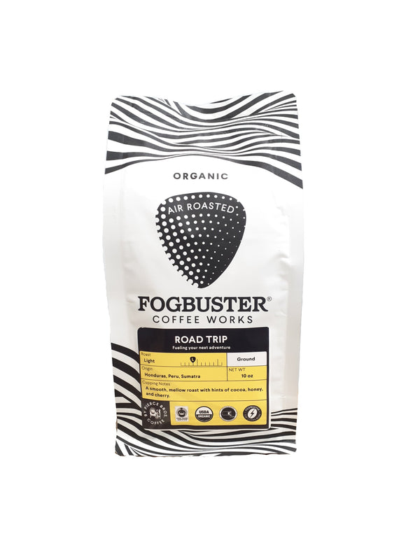 A white bag of Fogbuster® Coffee Works "Road Trip" organic air roasted Honduras coffee with zebra stripes, cocoa, honey, and nut notes; a smooth mellow roast; and a yellow label showing origin and roast level.