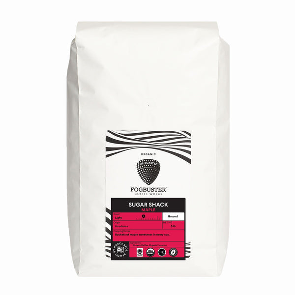 A white bag of Fogbuster® Coffee Works "Sugar Shack" features pink and black accents, a black coffee bean logo, and highlights maple sweetness in this premium Honduras organic coffee.