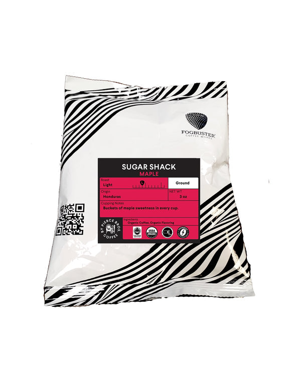 A white coffee bag with black zebra stripes and a pink label, Sugar Shack by Fogbuster® Coffee Works is a 12 oz light roast ground Honduras coffee featuring maple sweetness. The label has a QR code and prominent branding.