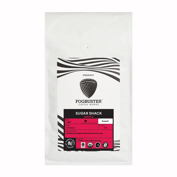 A white bag of Fogbuster® Coffee Works Sugar Shack ground coffee displays black and white wavy lines with a red label highlighting maple sweetness, roast level, and its Honduran origin on the front.