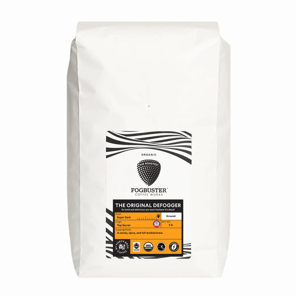 A white bag of Fogbuster® Coffee Works' The Original Defogger coffee features a black and white label with an orange section showing it's a super dark roast, ground, and exceptionally full-bodied.