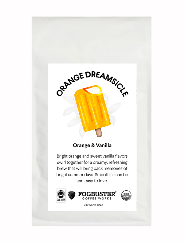 A "Orange Dreamsicle" coffee bag from Fogbuster® Coffee Works features an orange popsicle illustration and a label highlighting orange and vanilla notes in this light roast coffee.