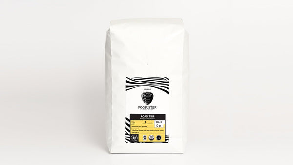 A white bag of coffee labeled "Fogbuster" and "Road Trip" prominently in the center, featuring black and yellow accents. The front of the label also includes weight information as 12oz (340g) and a description highlighting the origin and flavor notes of this premium, shade-grown coffee from Fogbuster® Coffee Works.