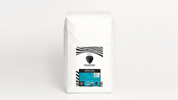 A white bag of Fogbuster Coffee Works' Air-Roasted Single Serve K-Cups, labeled "Moka Java," boasts a minimalist design with black wavy lines and an oval shield logo. The organic coffee, roasted using air-roasting technology, has a 5 out of 6 intensity and tasting notes of dark chocolate.