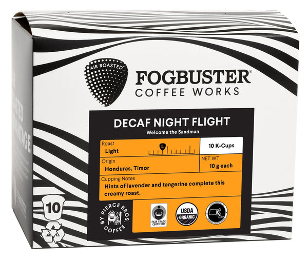 A white coffee packaging box labeled "Fogbuster® Coffee Works" contains the "Decaf Night Flight" blend with 10 single serve K-Cups. It features tasting notes of lavender and tangerine, is organic, fair trade certified, and originates from Honduras and Timor. The product is air-roasted for a gourmet experience and designed to be low acid.