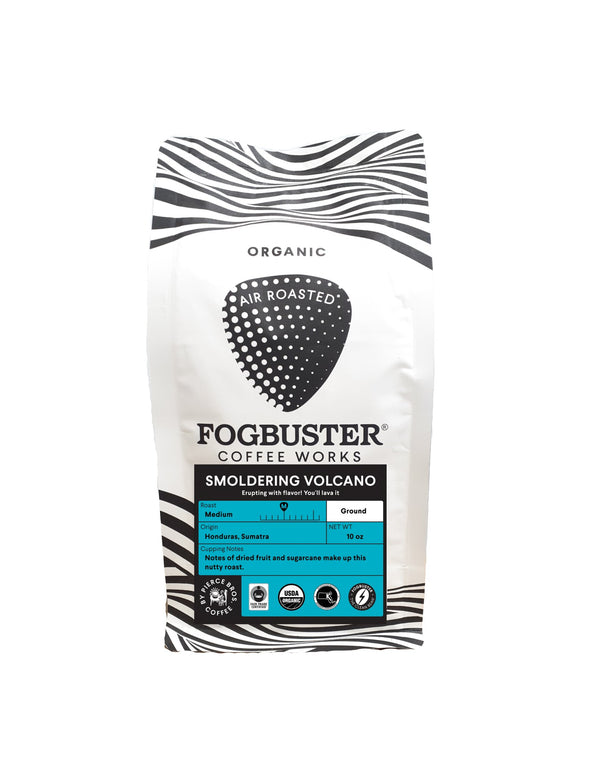 A white and black striped coffee bag labeled "Fogbuster® Coffee Works." The front text reads "Titanic: The Blend," "Organic Fair Trade coffee," "Air Roasted," and "Medium Ground 10 oz." Description notes flavors of dried fruit and spices. Various icons are displayed at the bottom.