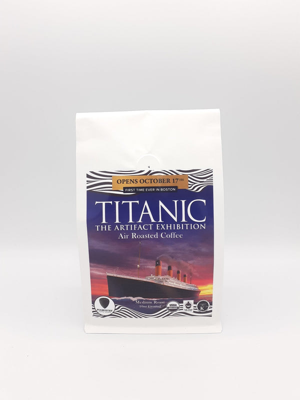 A white coffee bag from Fogbuster® Coffee Works labeled "Titanic: The Blend," featuring an image of the Titanic ship. Above, it reads "Opens October 17th, first time ever in Boston.